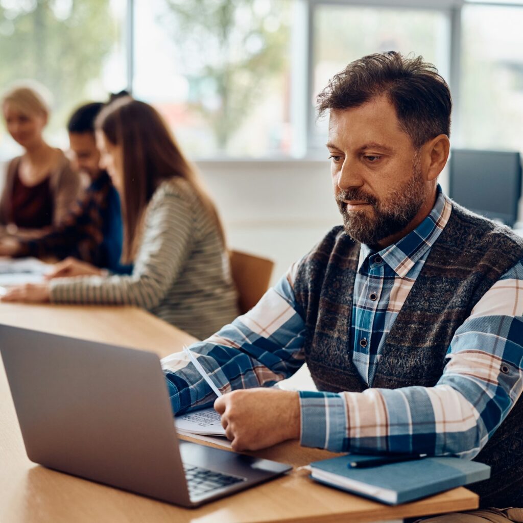 Mature student e-learning on laptop in the classroom.